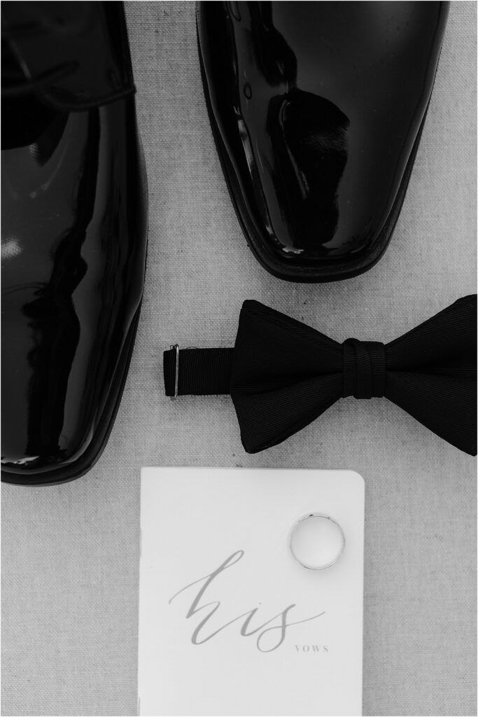 Grooms details of bowtie, vow book, ring and shoes