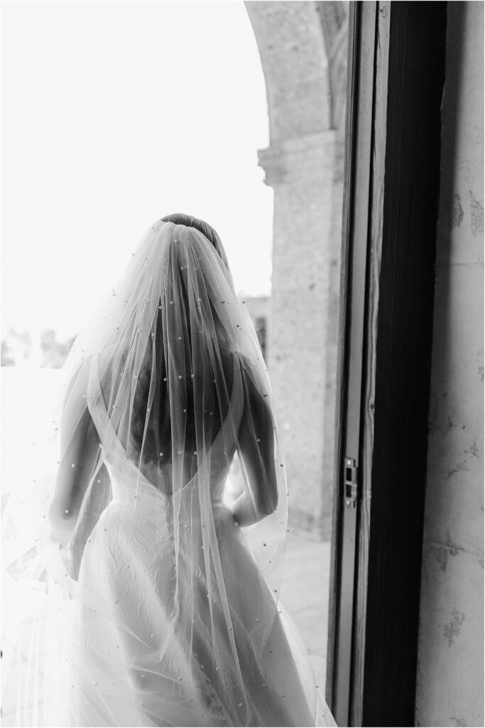 black and white photo of bride walking out with a pearl veil on